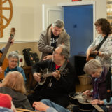 A group of people in the common area playing guitars amongst each other