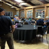 a man standing at the entrance of the dining hall watching people sitting in a circle with guitars